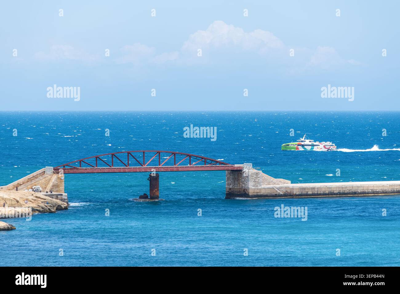 Valette, Malte – 16 mai 2025 : le pont rouge St Elmo enjambe l'entrée du port tandis que le catamaran Gozo Fast Ferry Your Wisdom traverse le Medit Banque D'Images