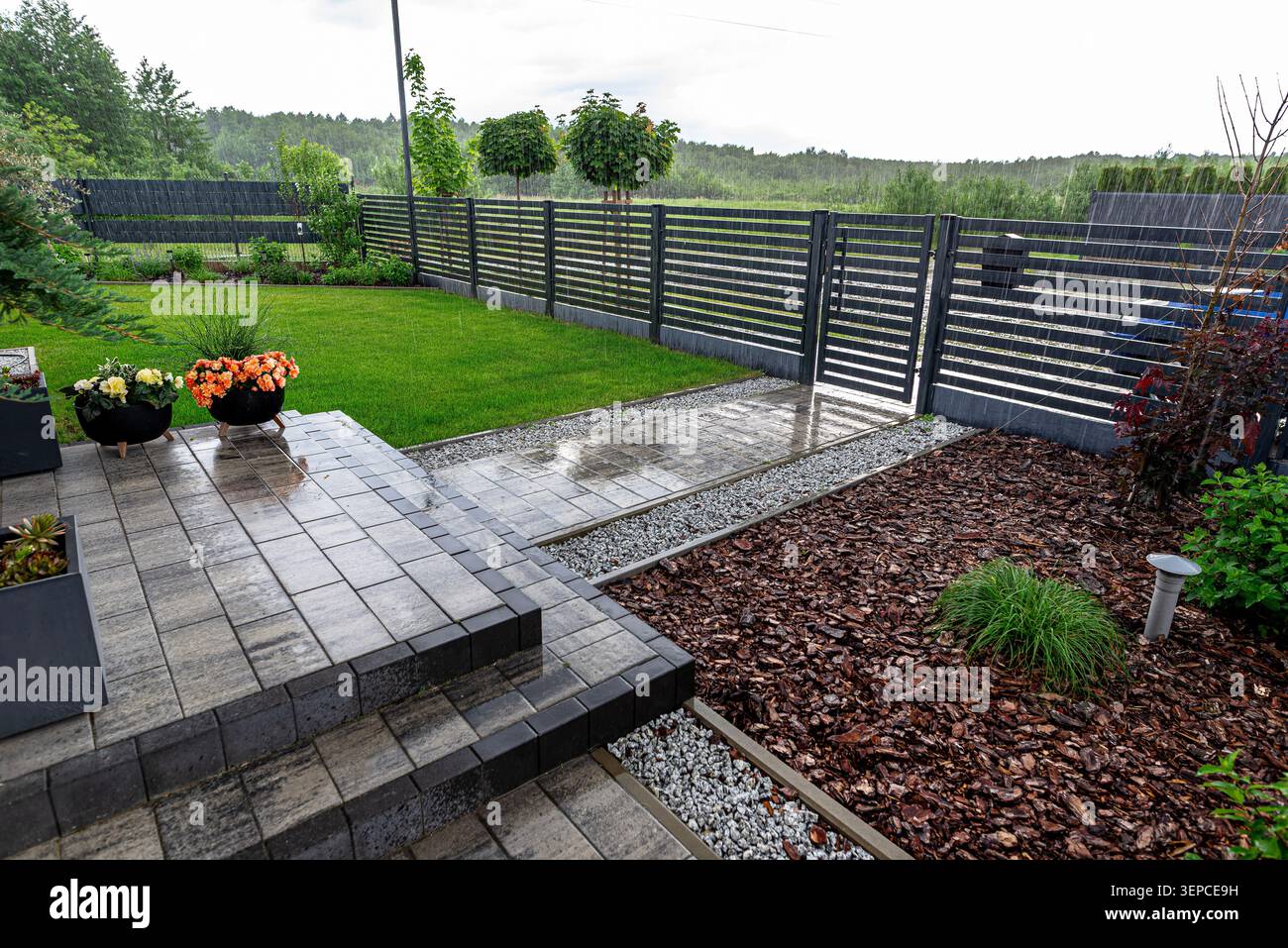 Gouttes de pluie tombant sur la terrasse pavée, la pelouse verte, le gravier et le paillis d'écorce Banque D'Images