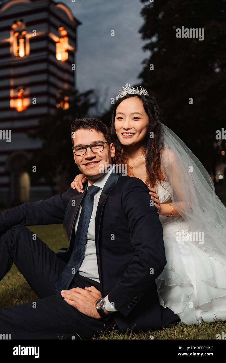 Couple de mariage interracial souriant tout en étant assis sur l'herbe Banque D'Images