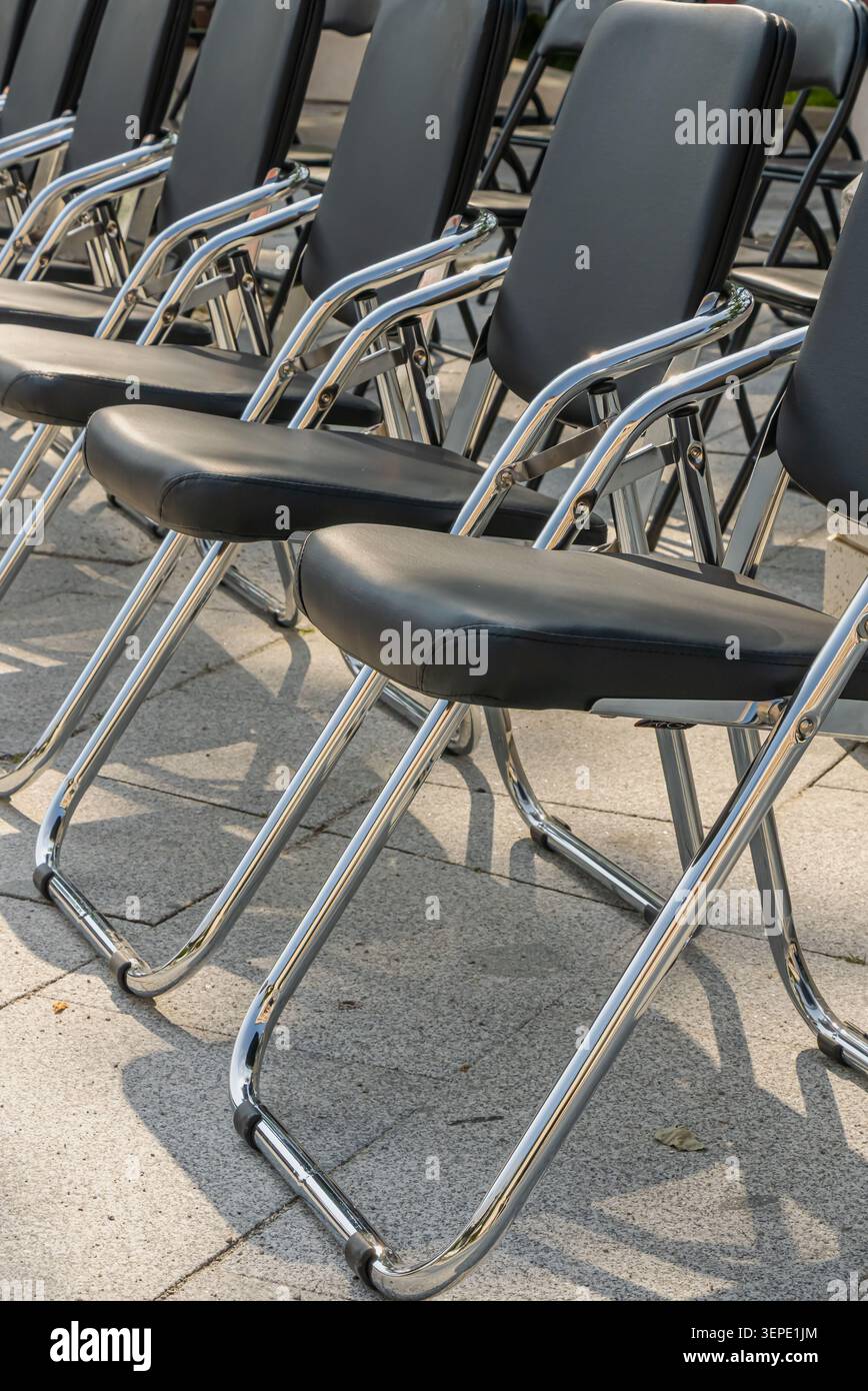 Les chaises pliantes noires sont soigneusement disposées en rangées dans un lieu extérieur, créant un motif géométrique fort adapté aux concepts d'événements et d'organisation Banque D'Images