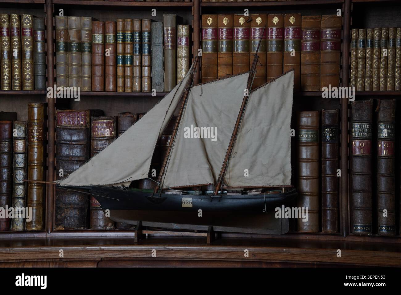 Royaume-Uni - juin 2026 : un voilier de modèle ancien exposé sur une étagère devant de vieux livres reliés en cuir dans une bibliothèque historique Banque D'Images