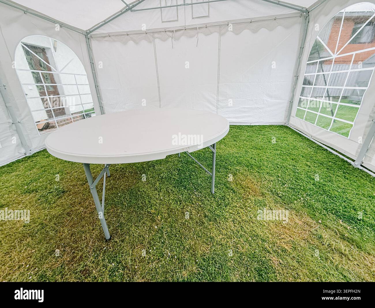 Smiltene, Lettonie - 12 juin 2026 : vue rapprochée d'une table pliante ronde à l'intérieur d'une tente de chapiteau blanche avec un sol en gazon naturel. Propre et polyvalent e Banque D'Images
