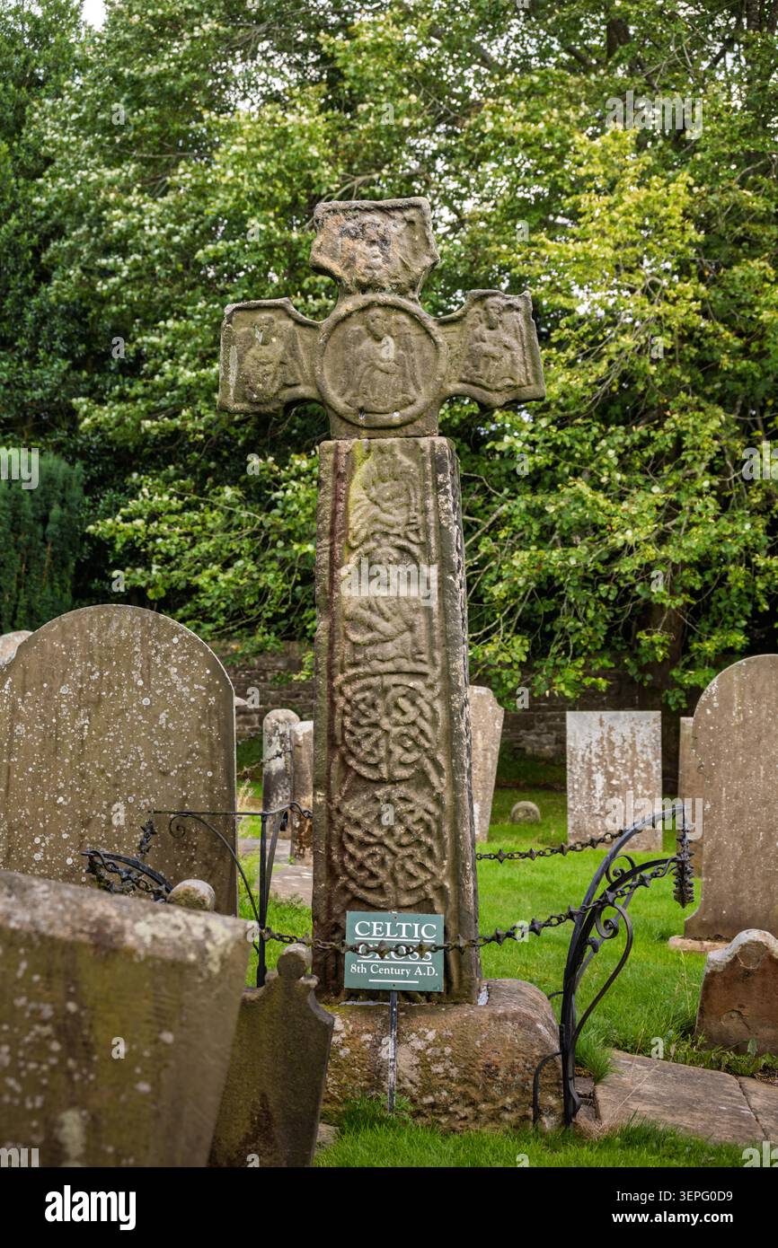 Vue portrait vertical de la célèbre croix de Saxe en pierre sculptée du VIIIe siècle debout parmi les vieilles pierres tombales dans le cimetière d'Eyam Banque D'Images