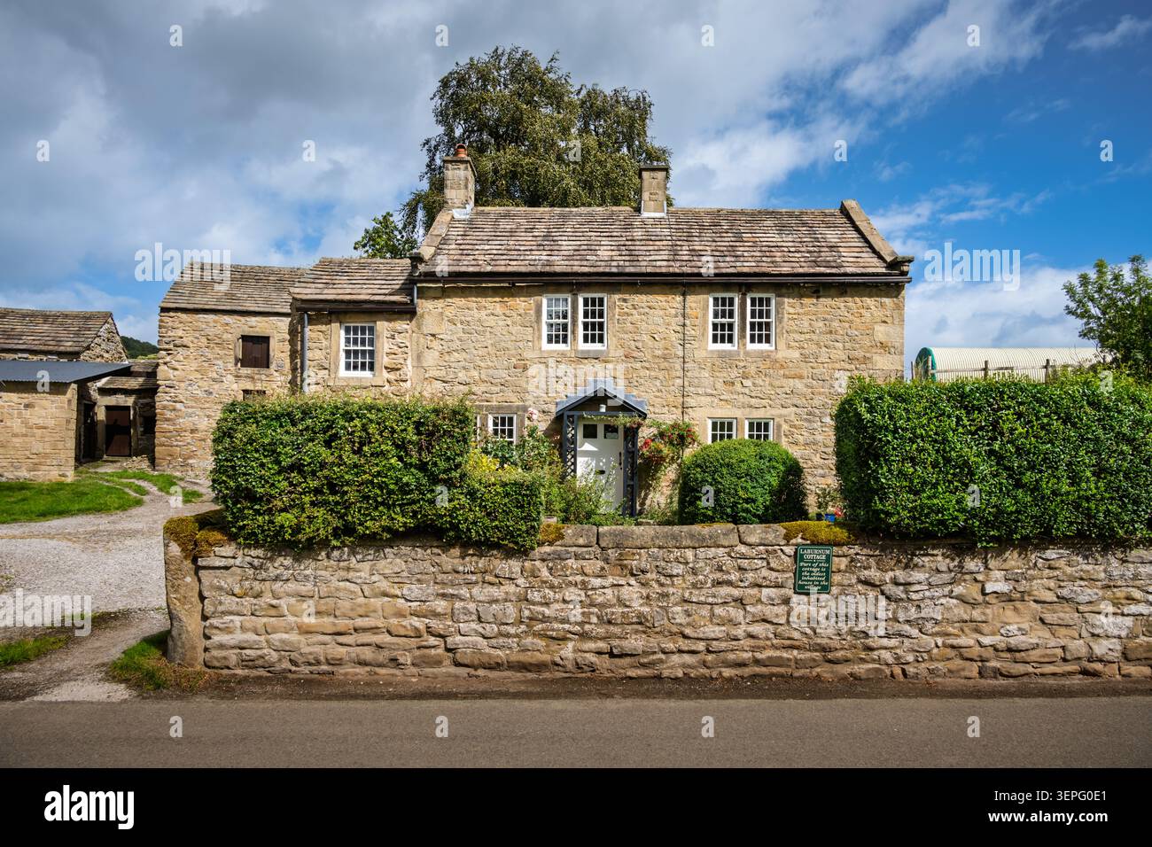 Vue en élévation de Laburnum Cottage, une maison résidentielle traditionnelle en gritstone avec une façade symétrique et des haies bien entretenues dans le village d'Eyam Banque D'Images