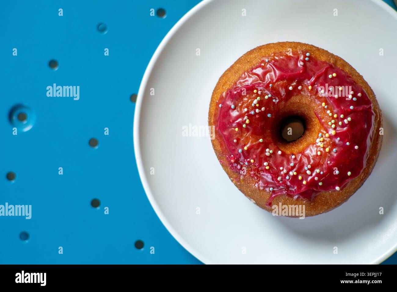 Un seul beignet émaillé rose sur une table bleue Banque D'Images