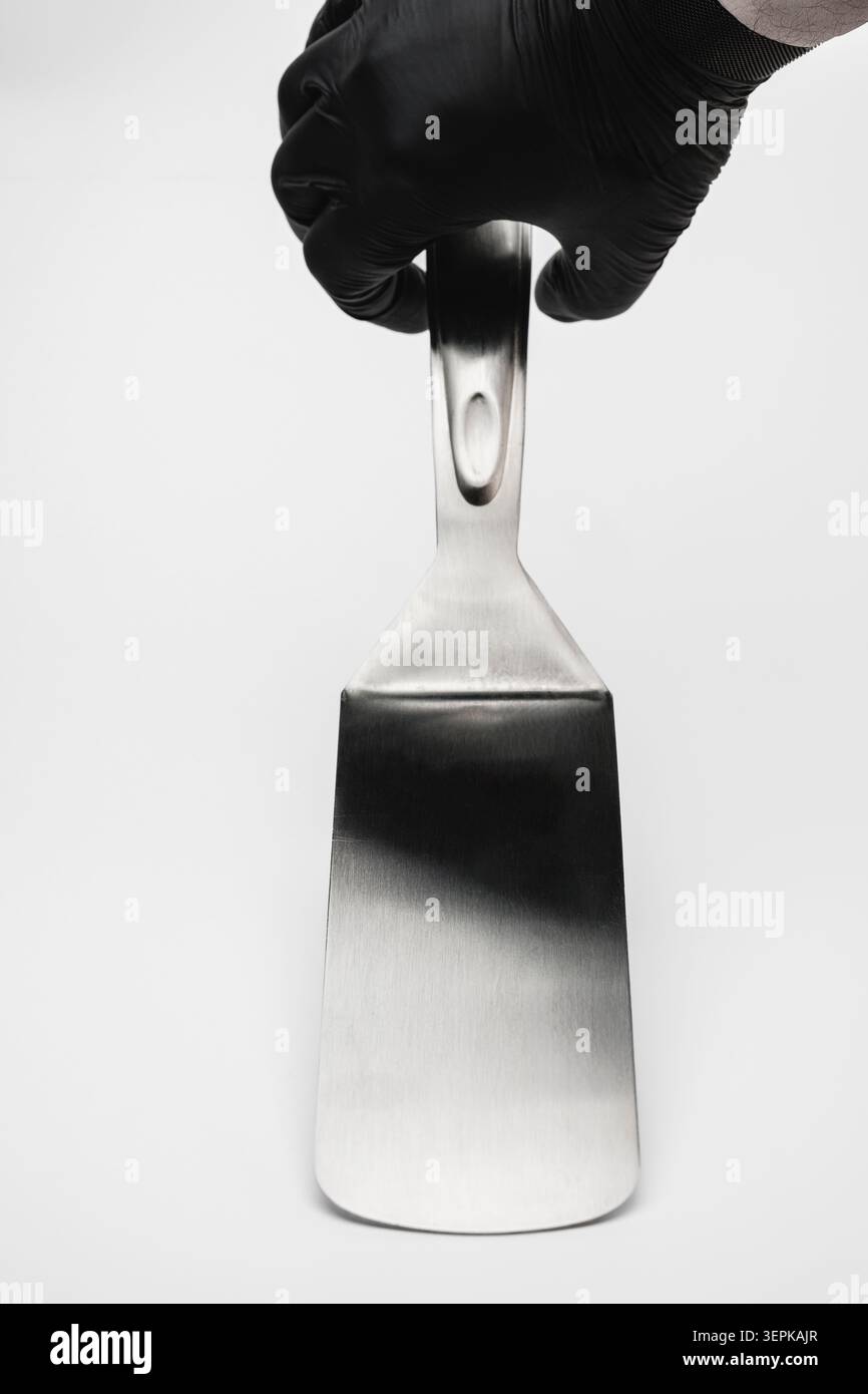 Chef portant un gant noir tenant la spatule en acier inoxydable Banque D'Images
