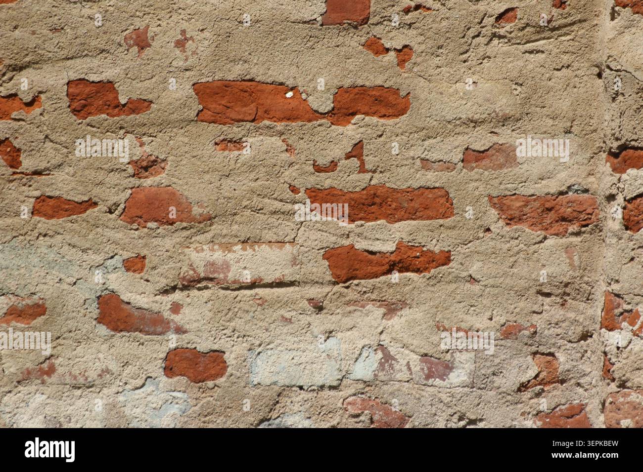 Plan plein format texturé d'un vieux mur de briques en décomposition avec plâtre brun exposant des briques d'argile rouge Banque D'Images