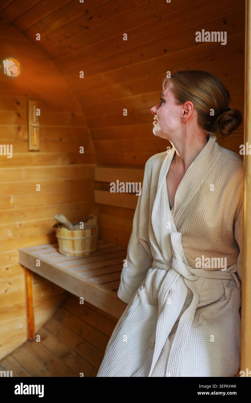 Concept de retraite de bien-être avec femme en peignoir à l'intérieur d'un sauna en bois, profitant du confort, de la tranquillité et de la récupération. Banque D'Images