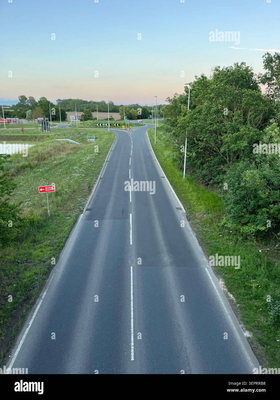 Une route moderne menant à un rond-point avec une signalisation claire sans entrée, entourée de verdure et éclairée par la lumière chaude du soir. - Image de stock capturée avec un smartphone