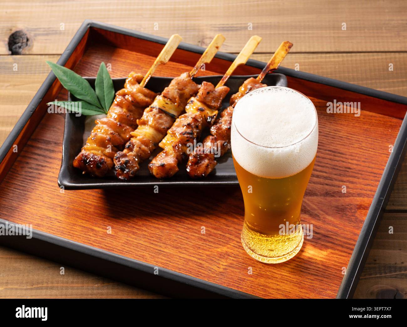 Verre de bière froide avec mousse moelleuse et brochettes de poulet japonais Yakitori sur plateau en bois Banque D'Images