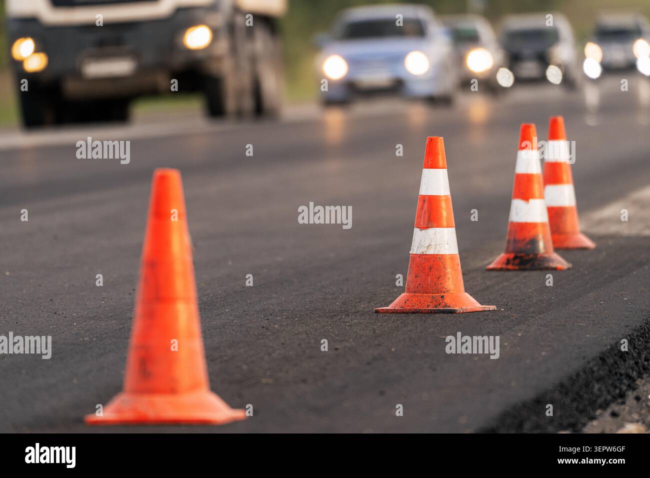 Travaux de réparation de routes avec revêtement d'asphalte frais et fermeture temporaire de la voie. Les véhicules passent près de la zone de construction. Concept de travaux routiers, trafic restric Banque D'Images