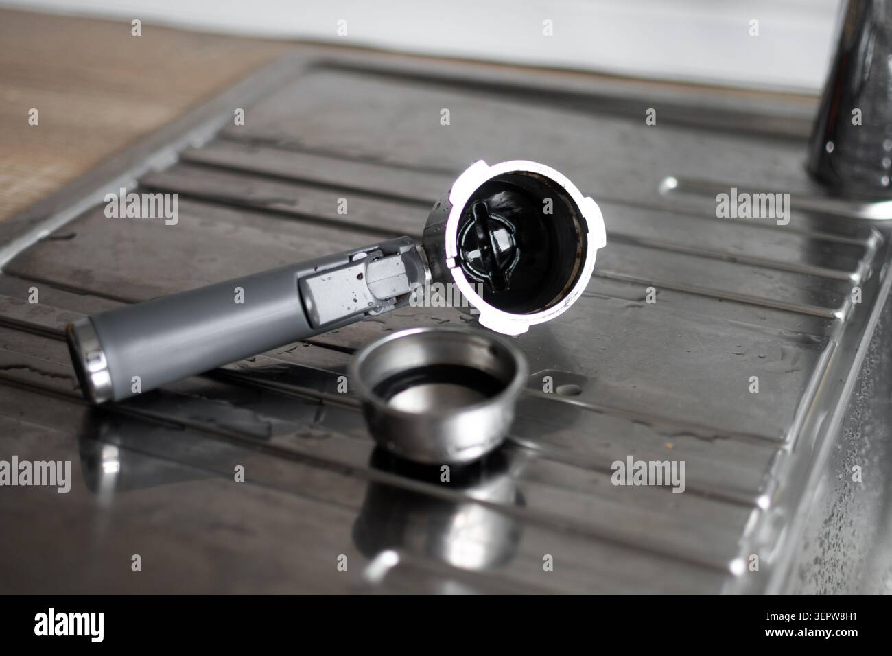 Gros plan d'un porte-filtre et d'un porte-filtre de machine à café placés sur un évier de cuisine en acier inoxydable après utilisation et nettoyage. Banque D'Images