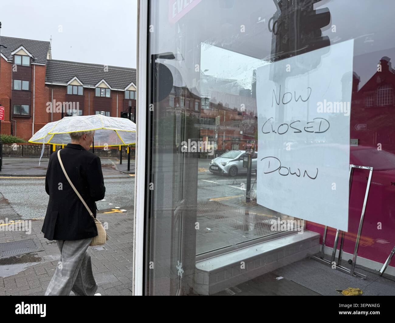 Ashton à Makerfield, Royaume-Uni. 16 juin 2026. Une femme traverse Ashton-in-Makerfield, la plus grande ville de la circonscription de Makerfield, sous la pluie. Jeudi, une élection partielle pour un siège au Parlement britannique aura lieu dans la circonscription de Makerfield, dans le nord-ouest de l'Angleterre. Le principal rival de Keir Starmer·au sein du parti, le maire de Manchester Andy Burnham, est candidat pour le Parti travailliste. Crédit : Patricia Bartos/dpa/Alamy Live News Banque D'Images