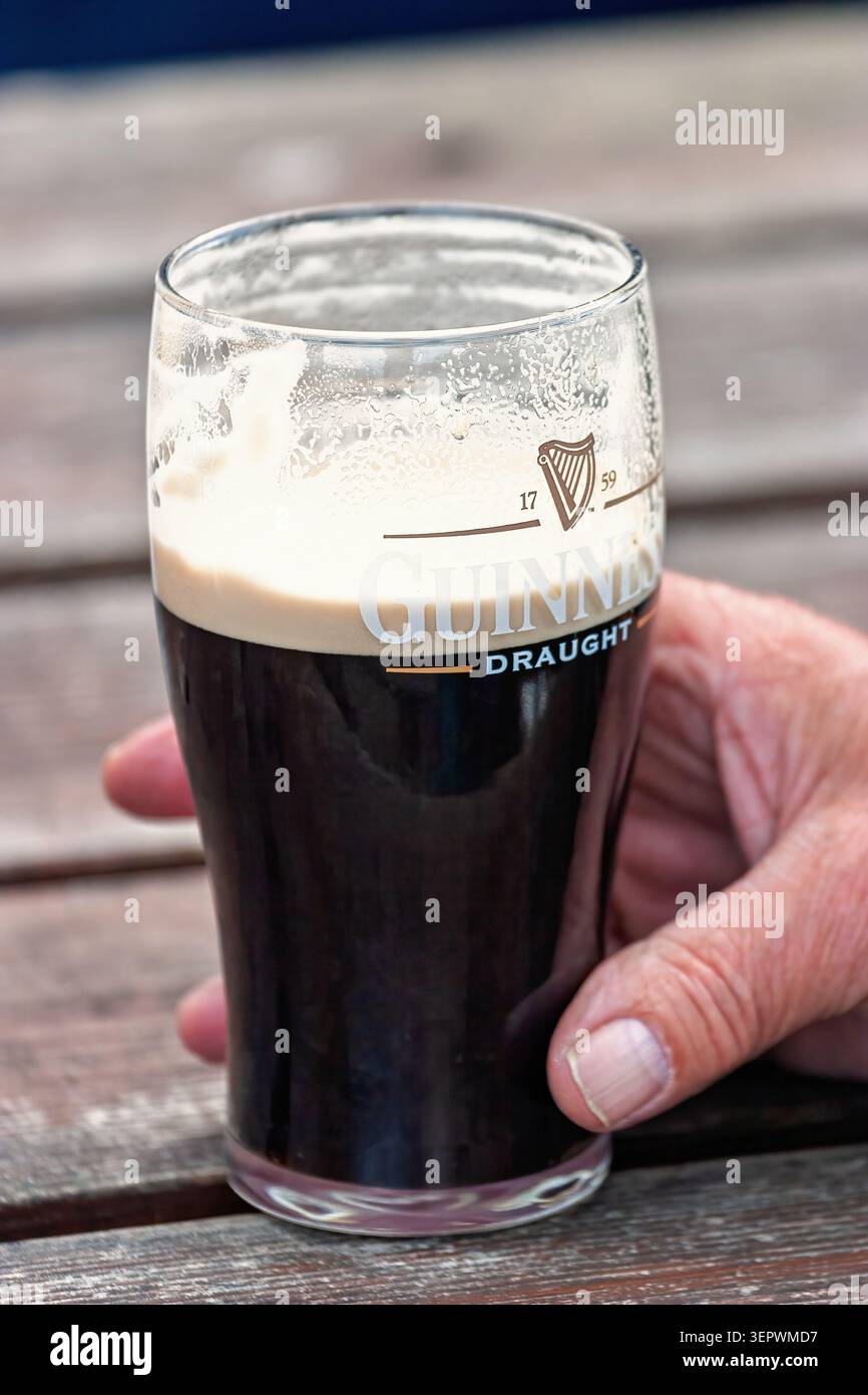 Main tenant une pinte de bière pression Guinness avec la tête crémeuse sur une table Banque D'Images