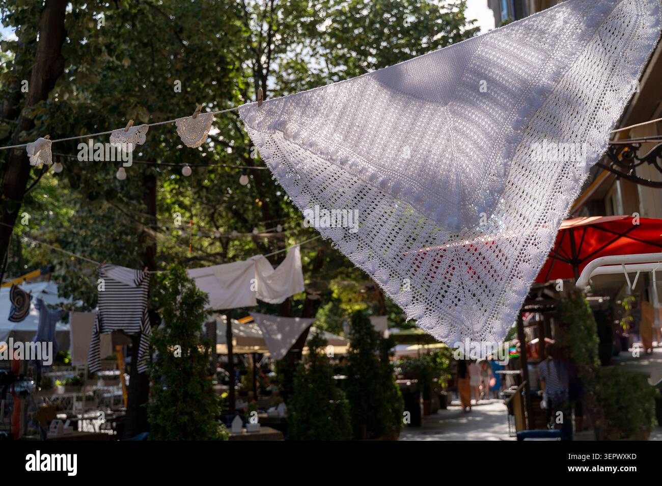 Mouchoirs en dentelle blanche suspendus à une corde dans une rue de la ville. Les textiles délicats créent une atmosphère romantique dans un café d'été. Concept de handcraf Banque D'Images