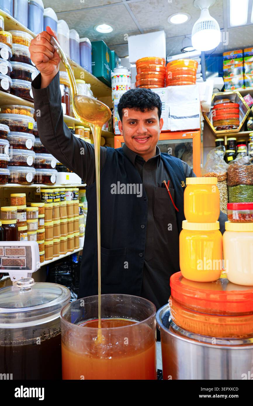 Sympathique marchand local versant du miel doré pur dans une boutique du vieux souq de Taif en Arabie Saoudite Banque D'Images