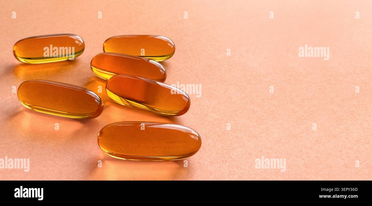 Capsules softgel jaunes translucides sur fond orange vif avec espace de copie. Concept moderne de santé holistique, médecine alternative, vitamine quotidienne Banque D'Images
