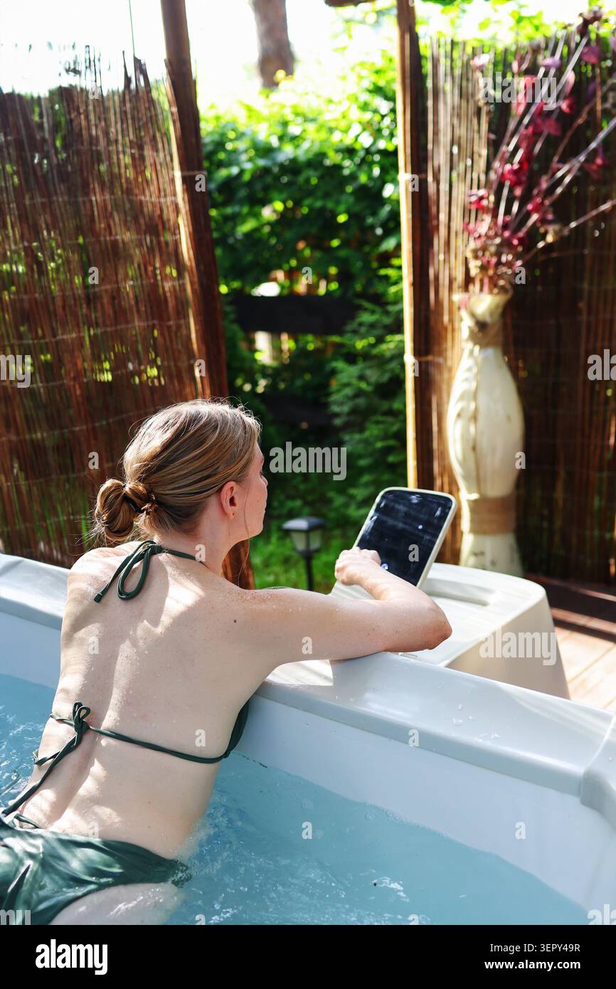 Invitée féminine se détendant dans un jacuzzi bouillonnant et utilisant un système de contrôle intelligent lors d'une expérience de retraite de bien-être de luxe. Banque D'Images