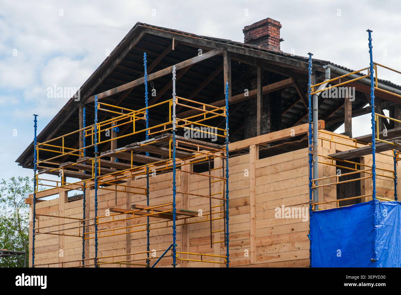 Les ouvriers remplacent les éléments en bois détériorés d'un ancien bâtiment en bois en utilisant des échafaudages lors de la restauration et de la réparation Banque D'Images