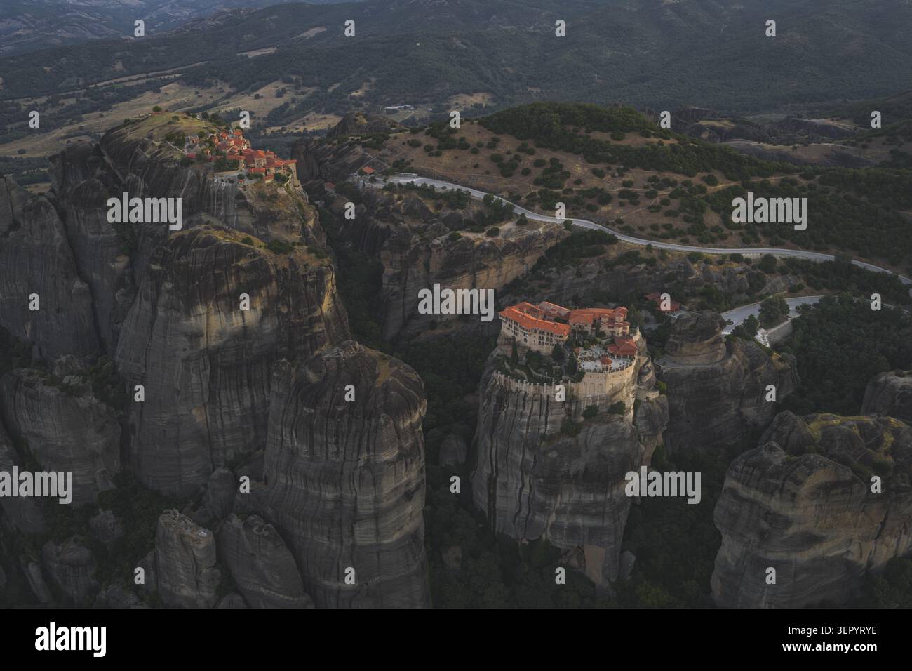 Vue aérienne des monastères historiques des Météores perchés au sommet d'énormes piliers rocheux entourés de collines verdoyantes et de routes sinueuses à Trikala, en Grèce. Banque D'Images