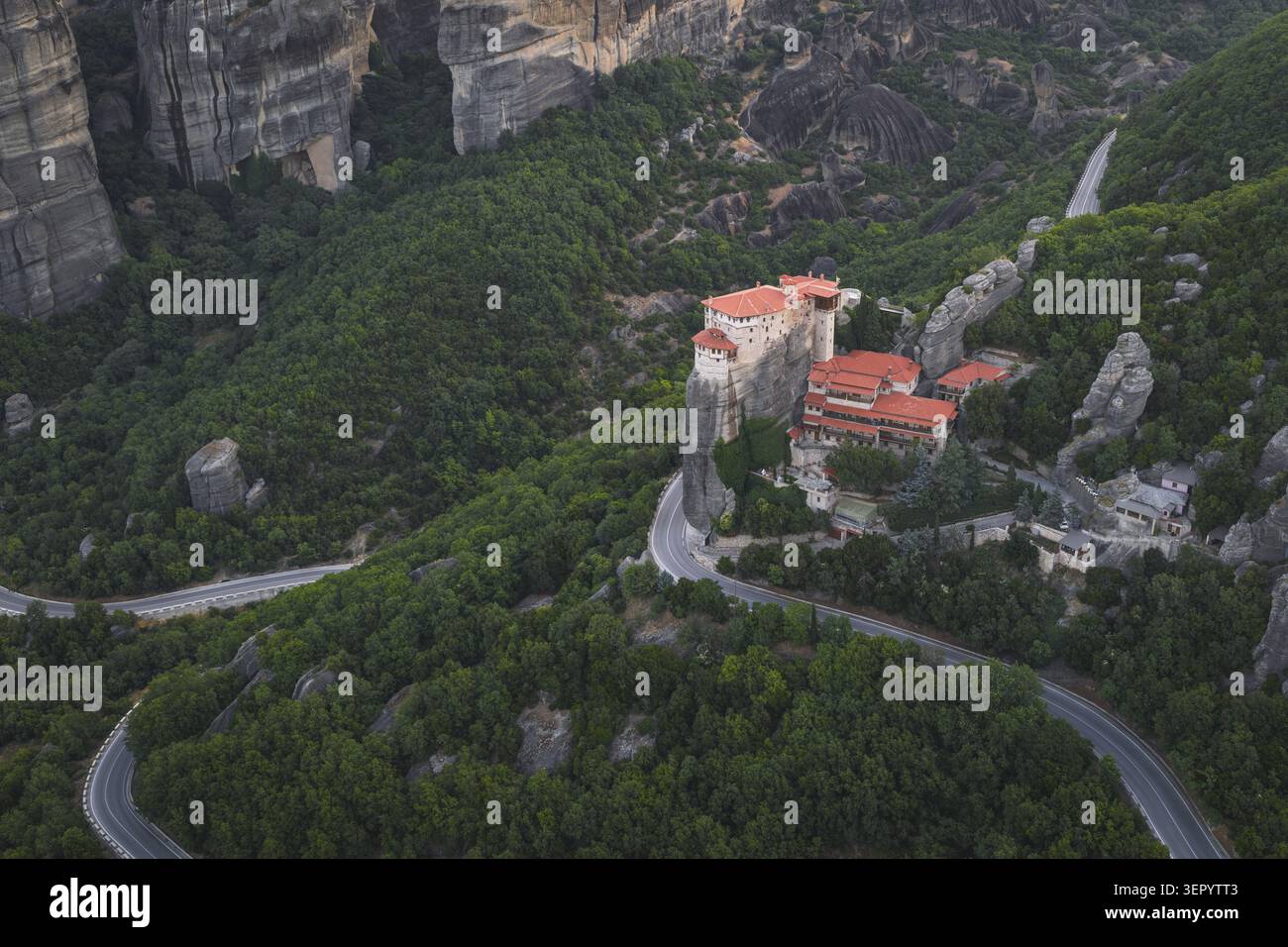 Vue aérienne du monastère de Rousanou aux Météores perché sur un pilier rocheux escarpé entouré de forêts verdoyantes et d'une route de montagne sinueuse à Tri Banque D'Images