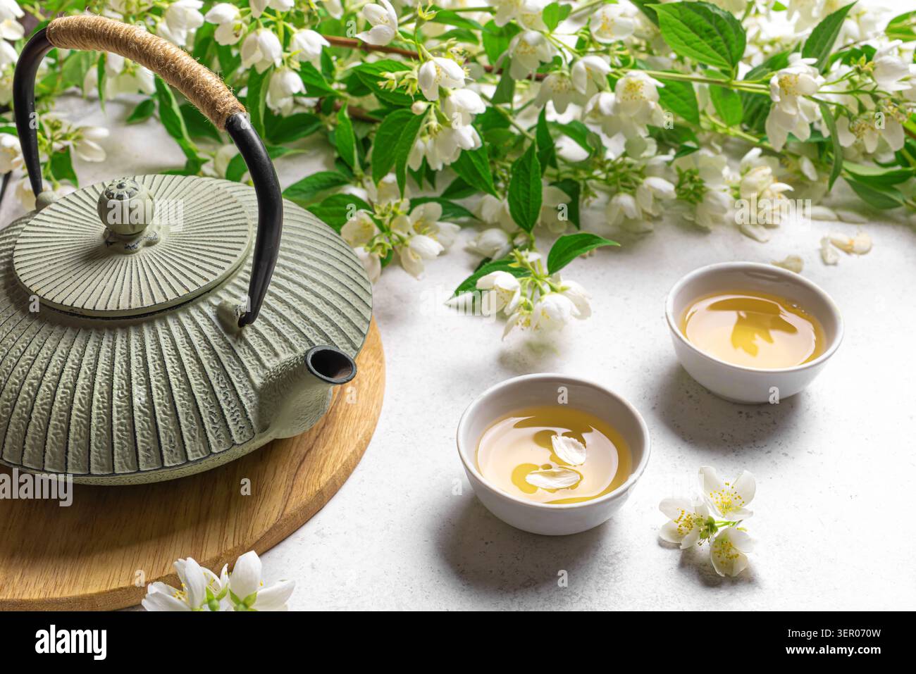 Thé vert japonais au jasmin dans une théière en fonte et des tasses à thé sur fond blanc en gros plan. Thé au jasmin naturel et branches florissantes. Banque D'Images