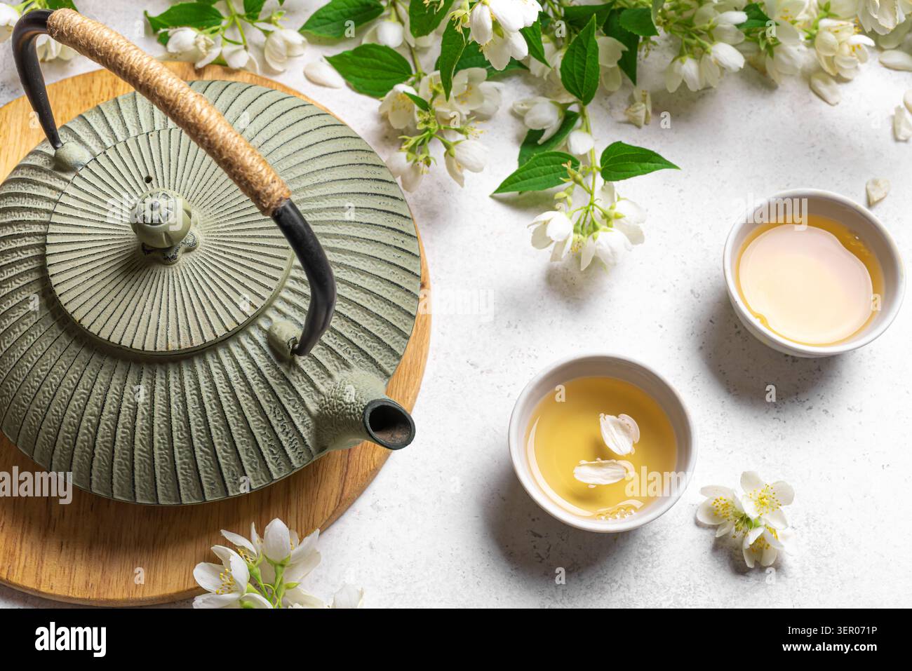 Thé vert japonais au jasmin dans une théière en fonte et des tasses à thé sur fond blanc en gros plan. Thé au jasmin naturel et branches florissantes. Banque D'Images