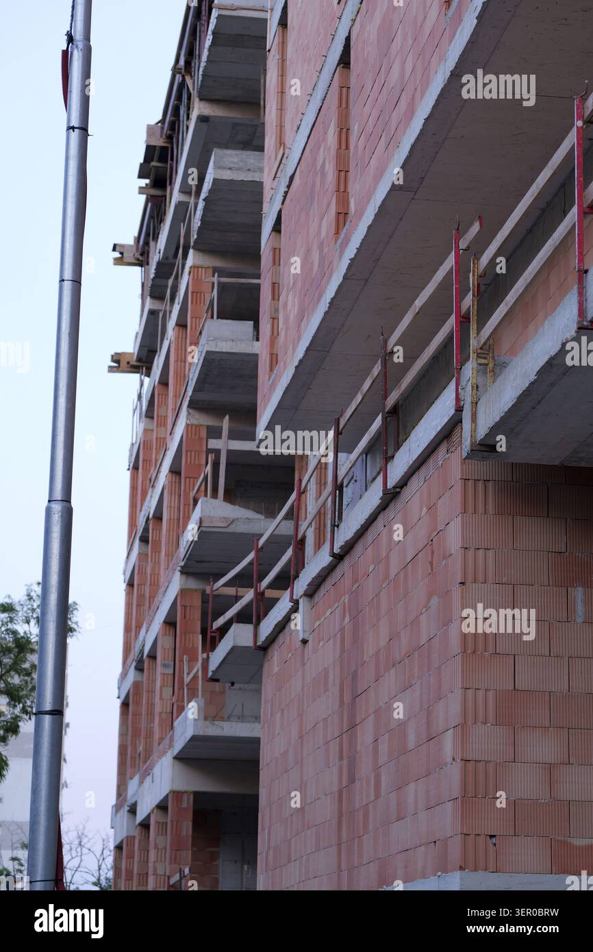Bâtiment à plusieurs étages en construction avec dalles de béton apparentes, formant balcons et planchers, le long de murs de briques creuses rouges, indiquant ongoin Banque D'Images