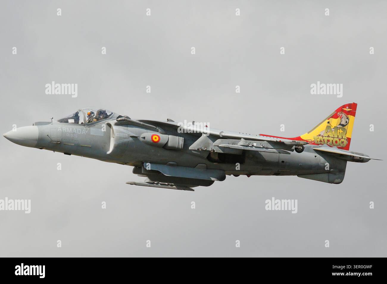 Un avion de saut AV-8B Harrier II de la marine espagnole avec une ailette arrière colorée et spécialement peinte vole horizontalement contre un ciel bleu clair. Banque D'Images