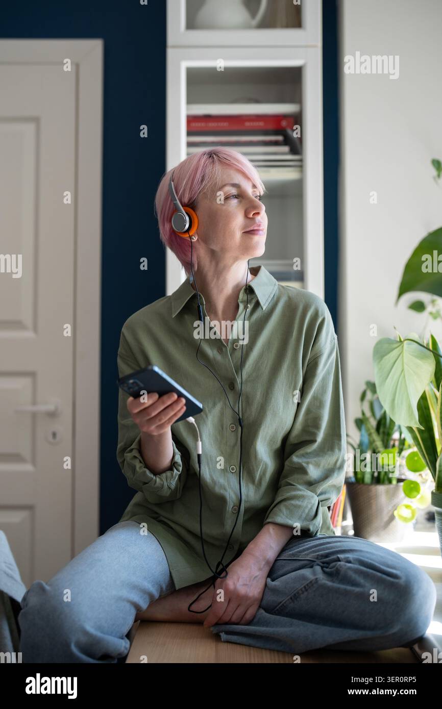 Femme mature détendue utilisant la musique en ligne à la demande plate-forme multimédia de streaming Web sur smartphone. Banque D'Images