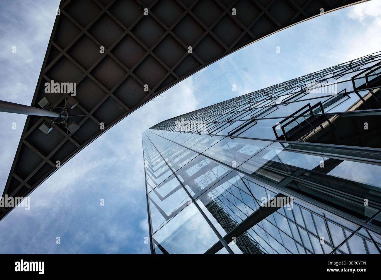Un grand bâtiment en verre se dresse contre un ciel bleu. La photo est prise de dessous, montrant la structure et les angles du toit. Settin urbain Banque D'Images