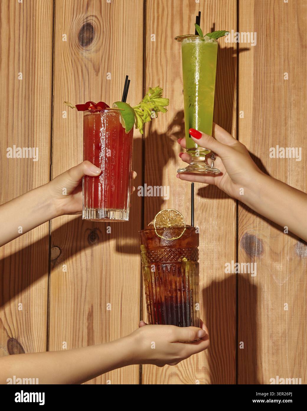 Mains tenant des cocktails rafraîchissants sur un fond de bois rustique, célébrant l'amitié et les bons moments Banque D'Images