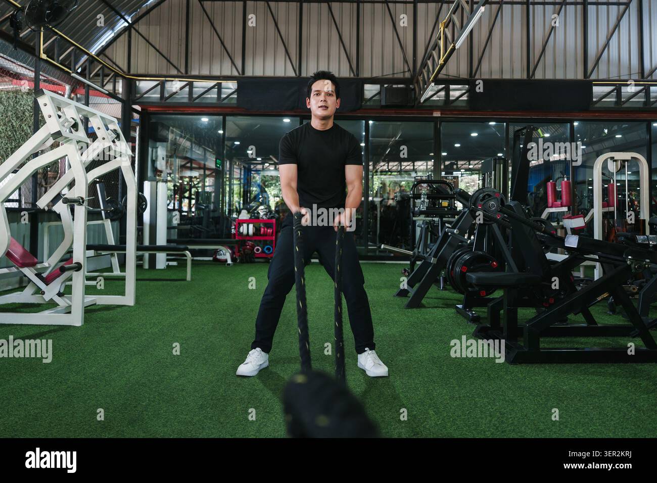 Homme asiatique déterminé effectuant des exercices de cordes de combat dans le gymnase pour l'entraînement de force et le style de vie actif de fitness Banque D'Images