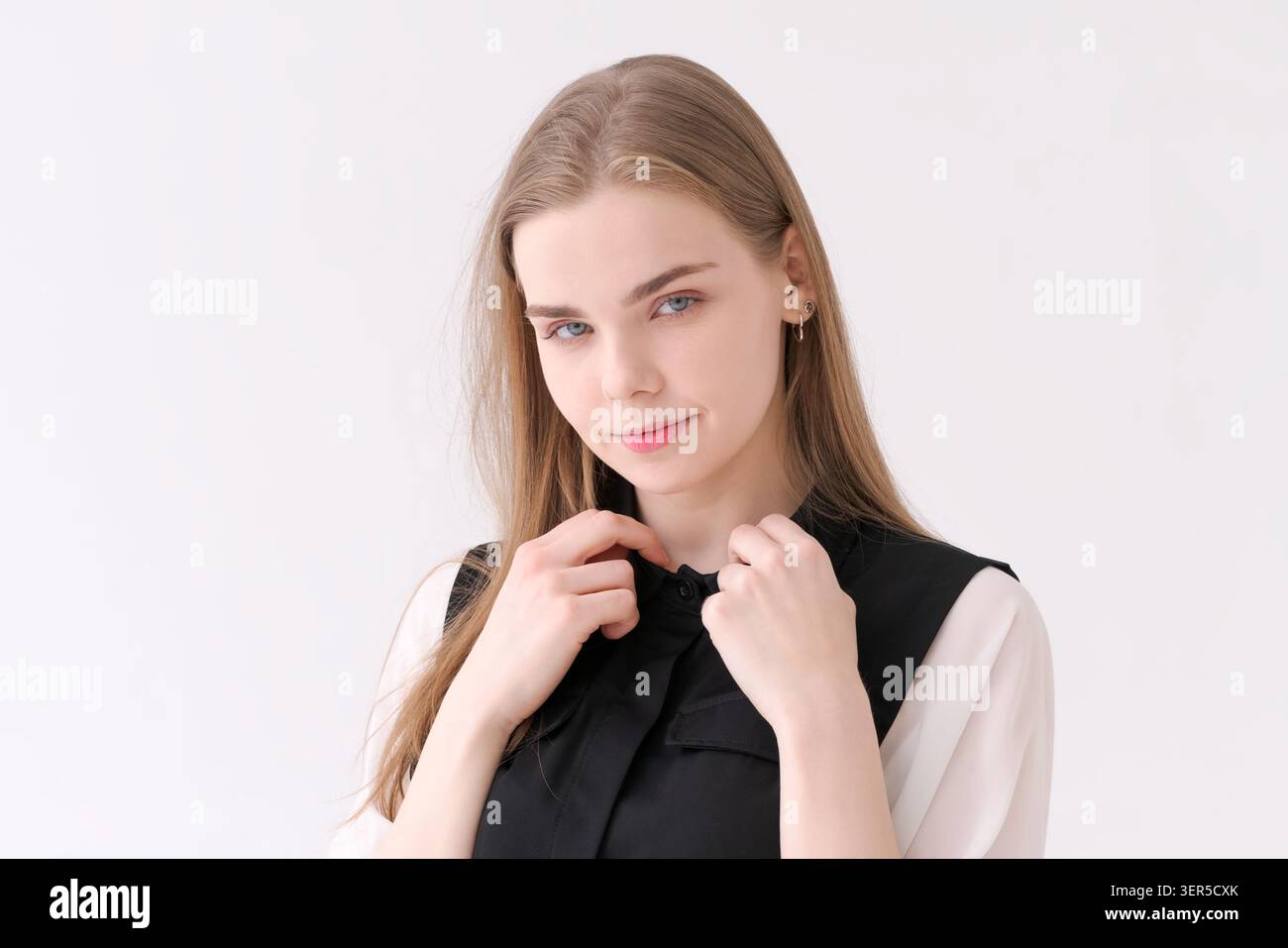 Une jeune femme blonde sympathique souriant doucement dans une combinaison noire et un chemisier blanc, un portrait de studio chaleureux et accessible Banque D'Images