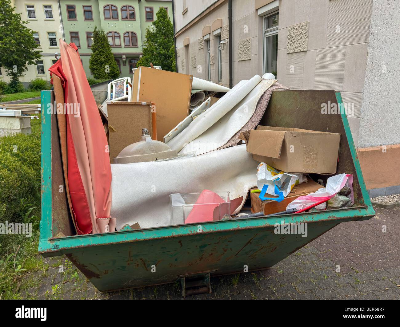 Conteneur vert rempli de déchets encombrants provenant d'un dégagement d'appartement, prêt pour le ramassage et le transport au centre de recyclage. Banque D'Images