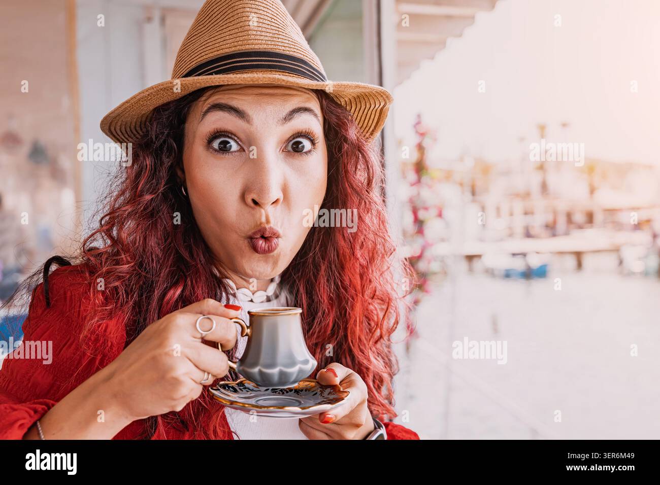 Jeune femme dans un chapeau de paille profitant des vacances, faisant un drôle de visage étonné tout en dégustant du café turc traditionnel Banque D'Images