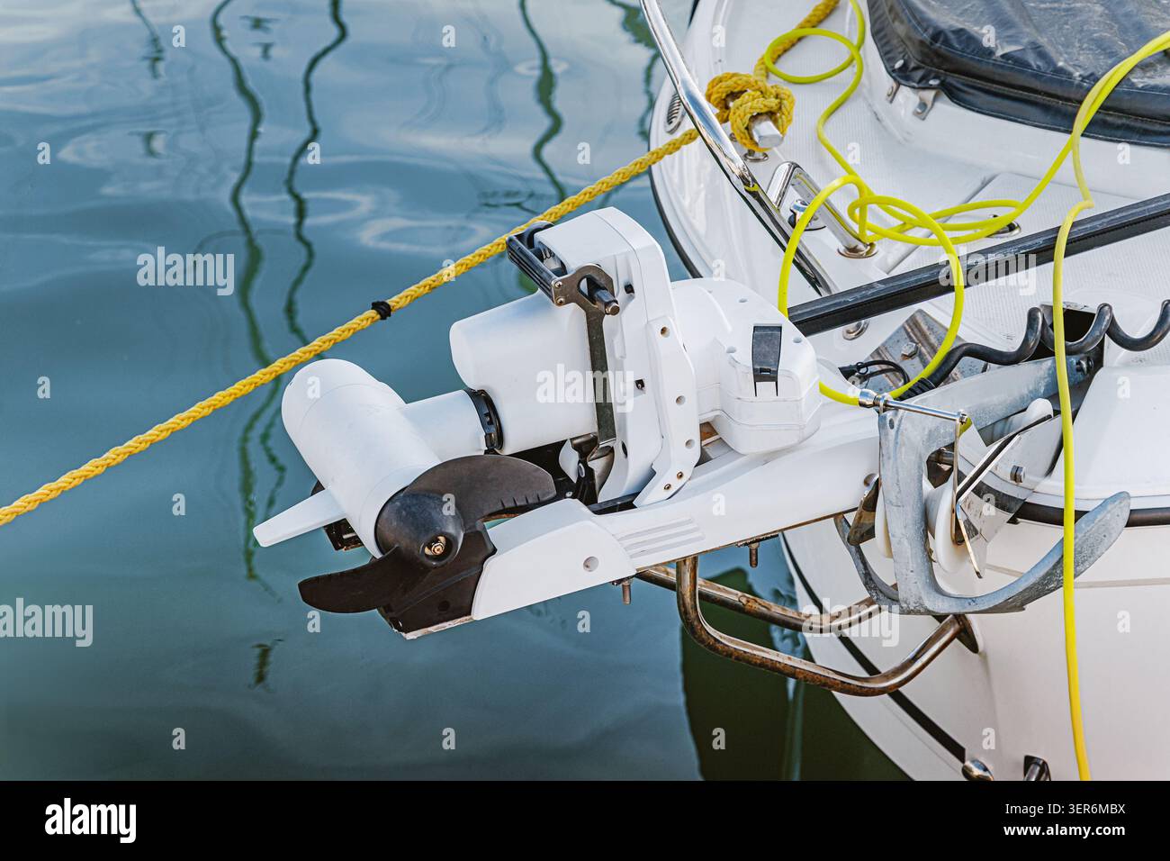 Moteur électrique blanc monté sur la proue d'un bateau avec une ancre, un câble d'alimentation et une corde visibles sur le pont Banque D'Images
