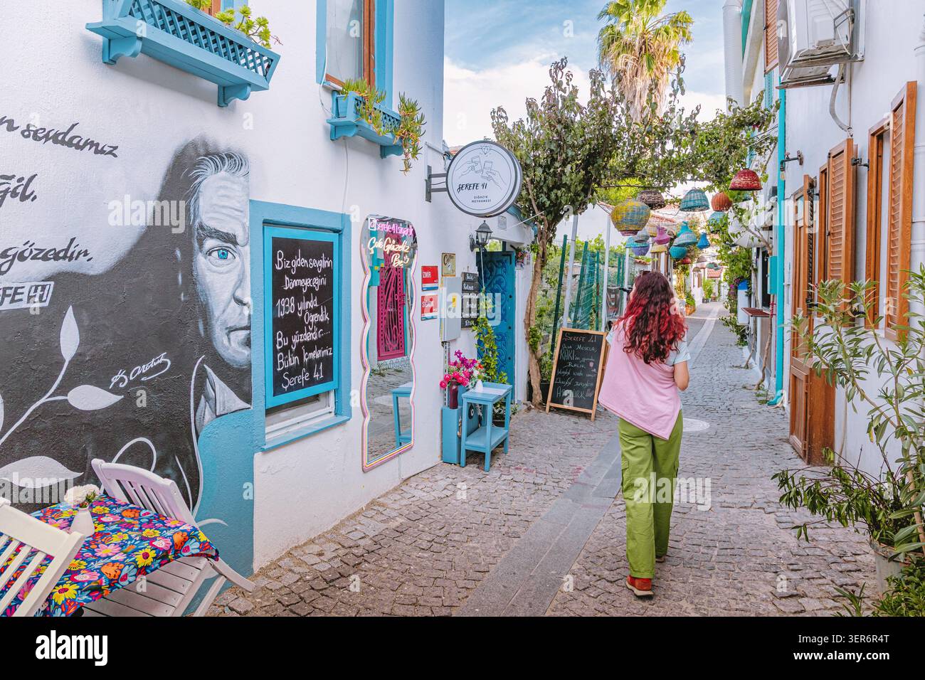 13 mai 2026, Sigacik, Turkiye : femme marchant dans une charmante rue pavée, avec une fresque murale Mustafa Kemal Ataturk et un archi méditerranéen dynamique Banque D'Images