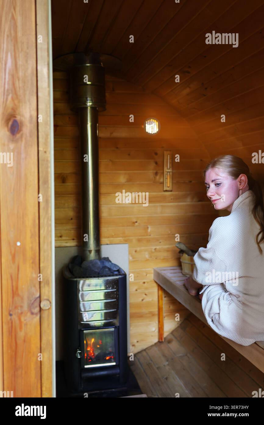 Femme détendue en peignoir debout à l'intérieur d'un sauna, embrassant un mode de vie sain, bien-être et thérapie thermale. Banque D'Images