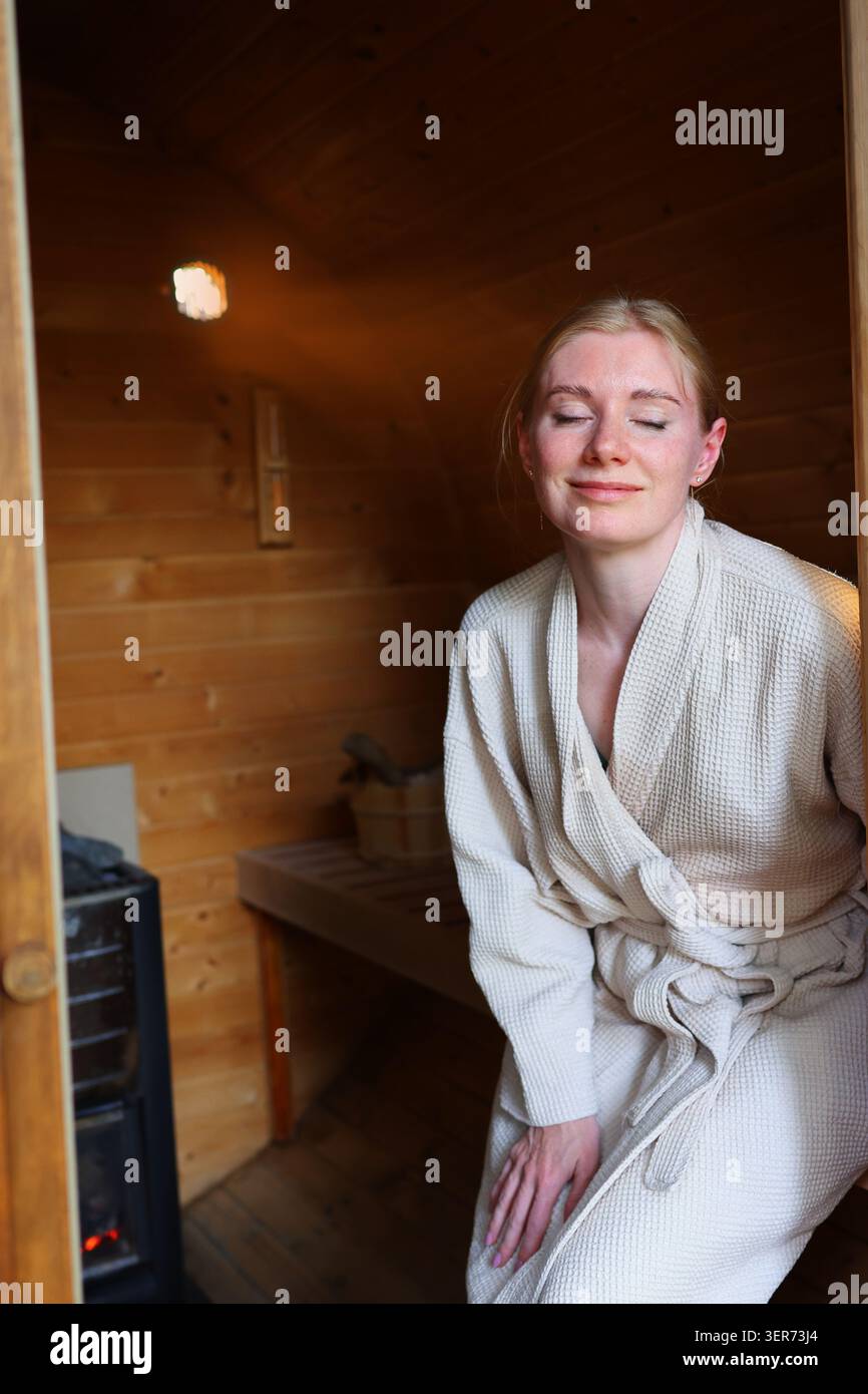 Jeune femme se reposant dans une cabine de sauna confortable, embrassant la thérapie thermique, la relaxation et les avantages d'un mode de vie sain. Banque D'Images