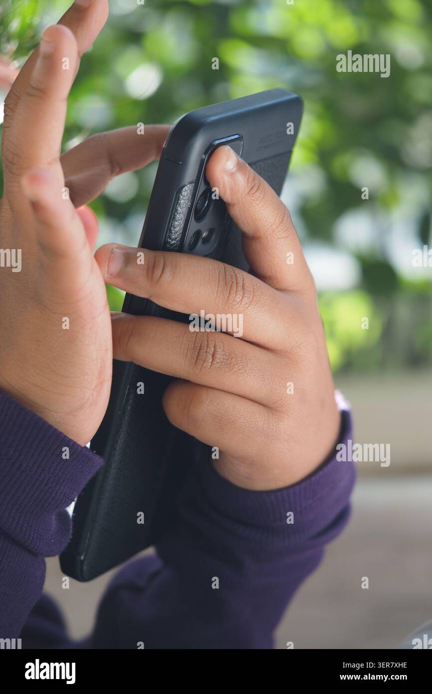 L'enfant regarde le téléphone lorsqu'il est assis à l'extérieur sous les arbres Banque D'Images