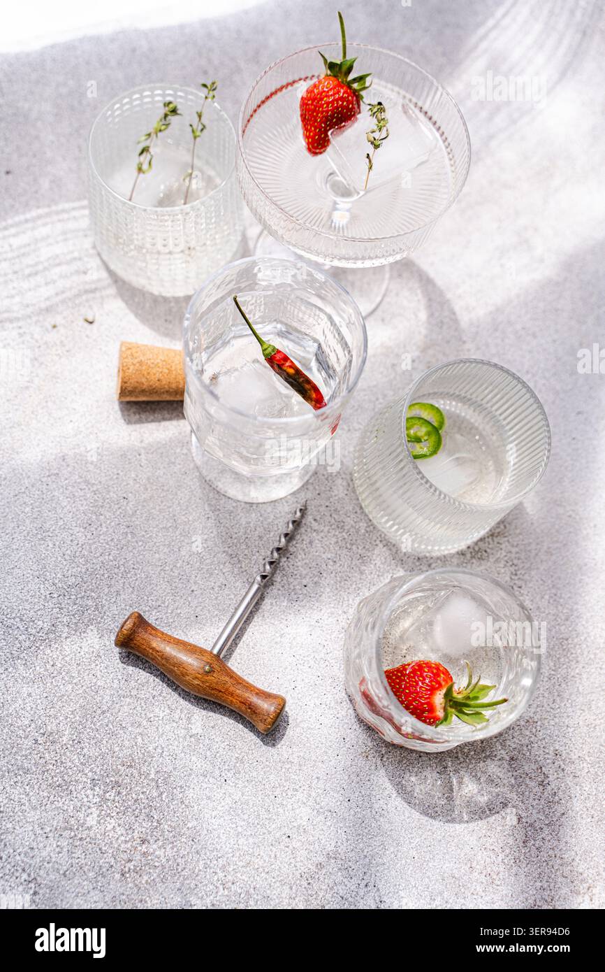 Cocktail de champagne d'été lumineux avec verres en cristal, glace et liège sur la surface de pierre, garni de fraise, de piment, de thym et de citron vert i. Banque D'Images