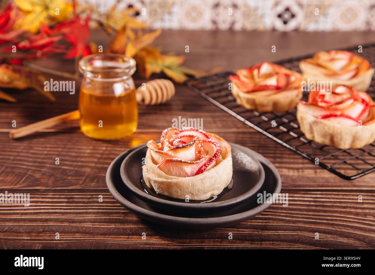 Élégants desserts aux pommes en forme de rose cuits à la perfection dorée, habilement disposés sur une table en bois rustique. Accentués d'un pot de miel, ces gâteries pro Banque D'Images