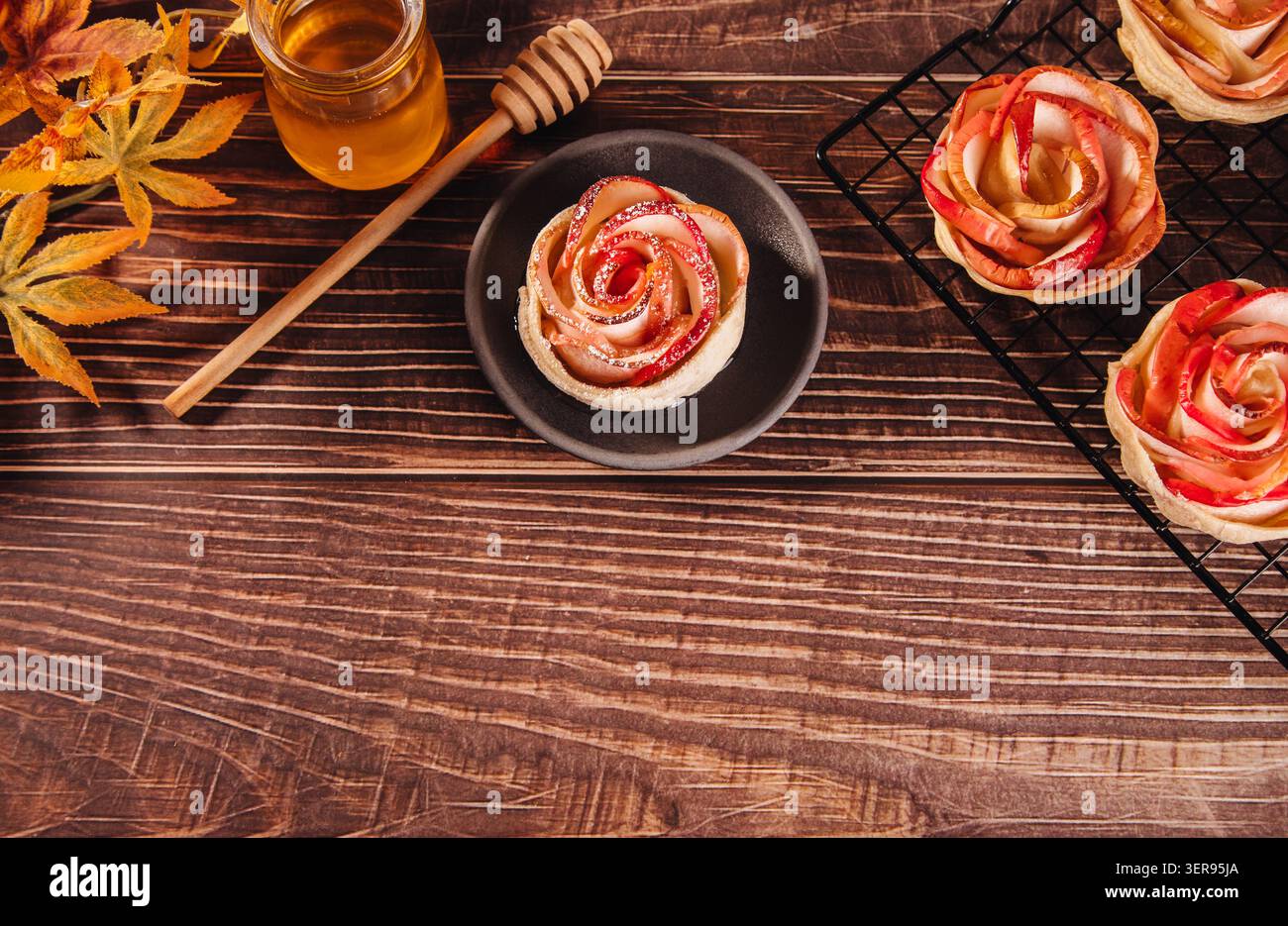 Un dessert aux pommes en forme de rose magnifiquement conçu se trouve sur une table rustique en bois. Entouré d'un pot de miel et de feuilles d'automne, ce gâteau cuit au four compromet Banque D'Images