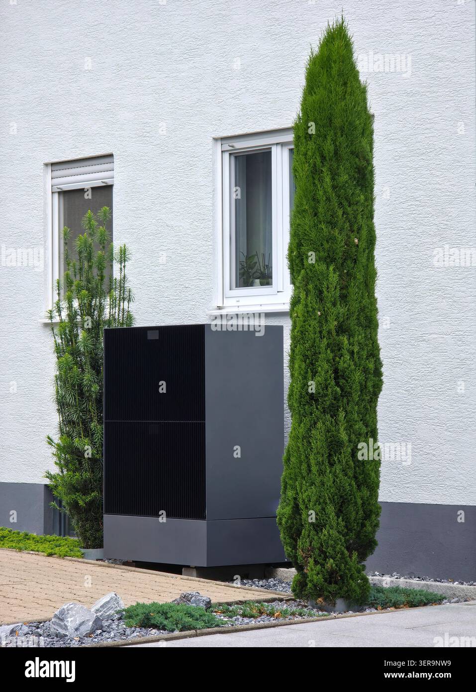 pompe à chaleur moderne efficace installée à côté de la maison traditionnelle améliorant le chauffage durable avec de la verdure Banque D'Images