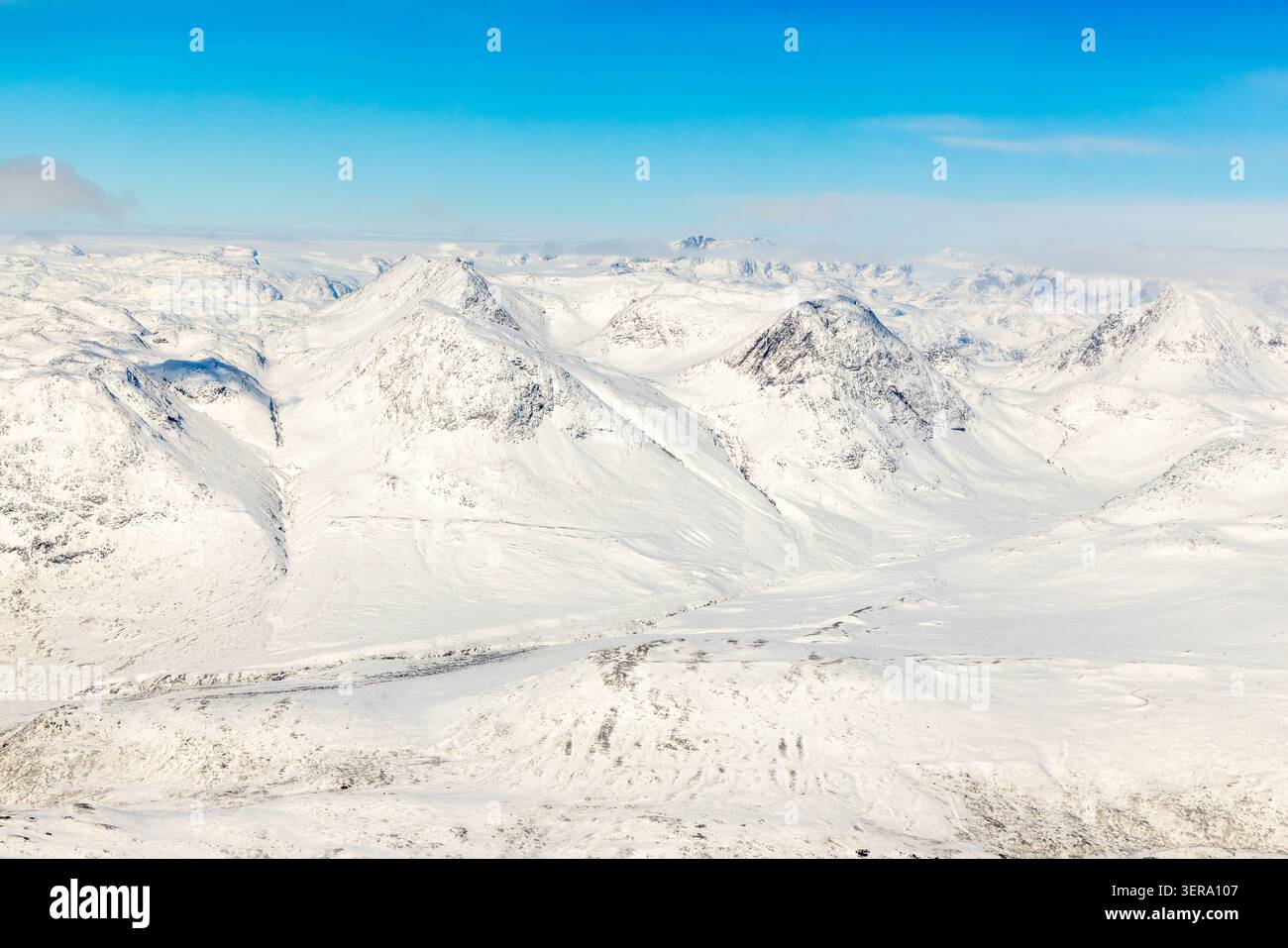 Vue aérienne de la chaîne de montagnes arctiques enneigées, des vallées gelées et de la calotte glaciaire sauvage du Groenland sous le ciel bleu, Groenland méridional, Groenland Banque D'Images