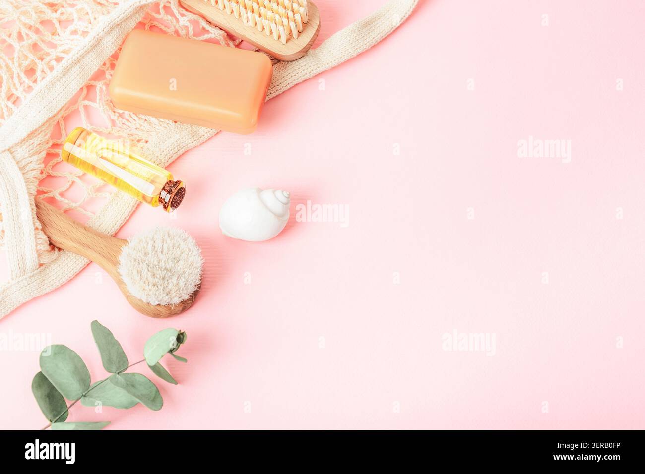 Accessoires de spa naturels avec savon, brosse corporelle, huile essentielle et branche d'eucalyptus sur fond rose avec espace copie. Vue de dessus, pose à plat. Banque D'Images
