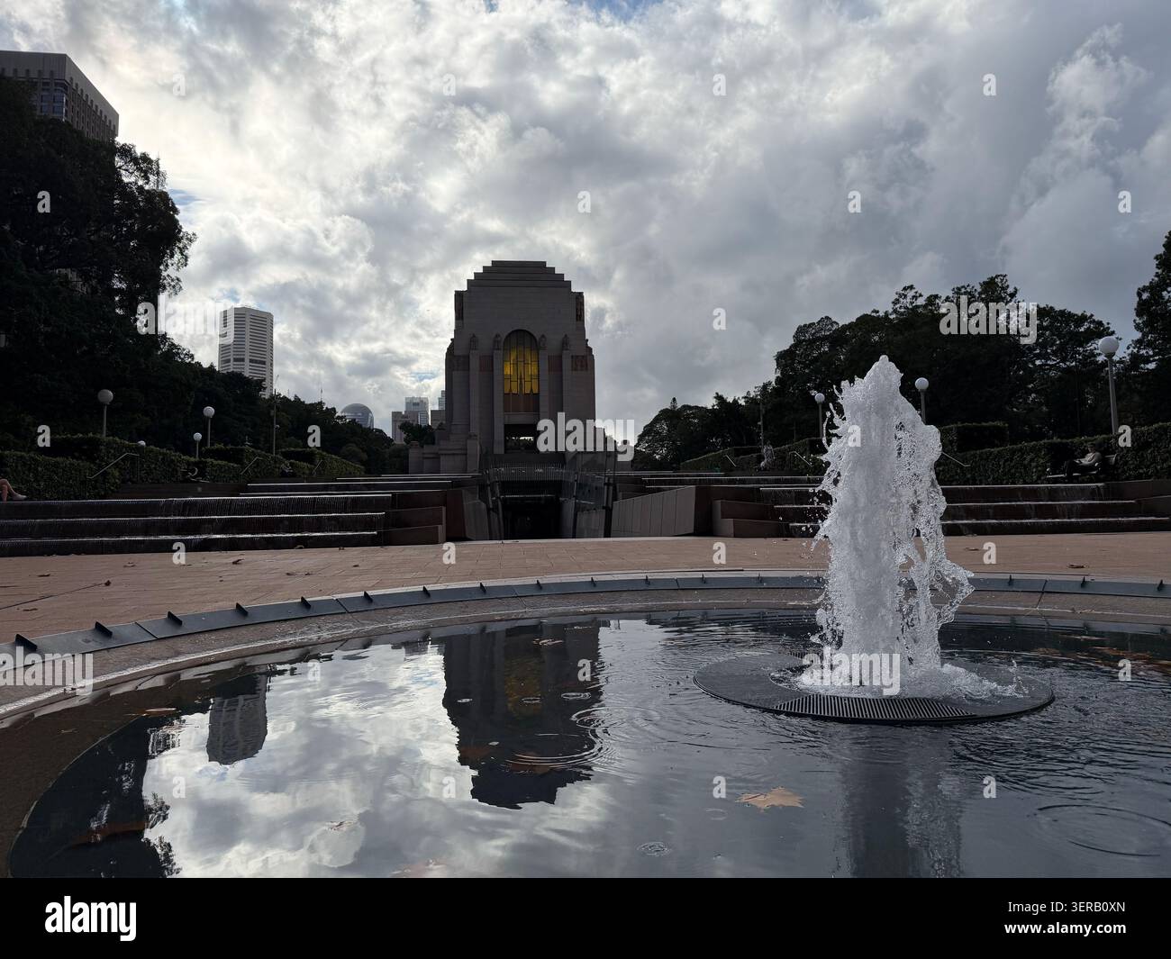 L'ANZAC Memorial à Hyde Park, Sydney, brille par une lumière intérieure chaude derrière un jet de fontaine et une cascade d'eau sous un ciel couvert. Banque D'Images
