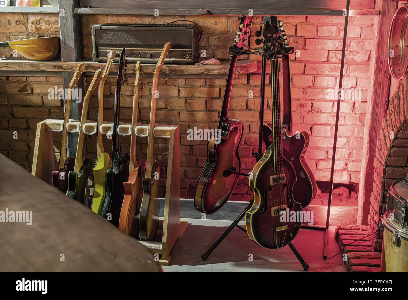 Guitares et basses affichées bien en évidence sur un stand en bois, présentant une variété de finitions et de formes en bois, avec amplificateur de style vintage sur l'étagère abo Banque D'Images