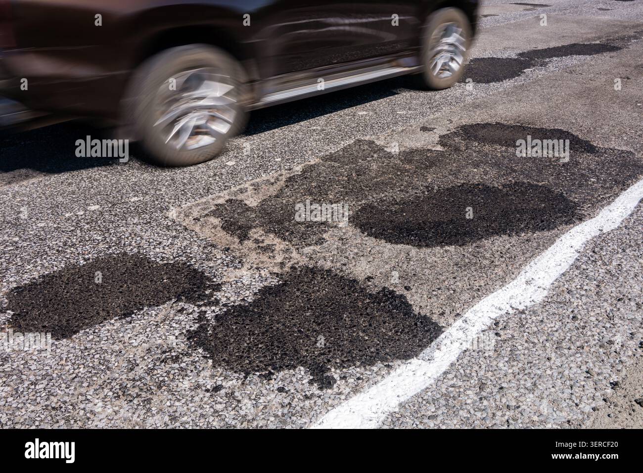 Voiture conduisant sur une route avec plusieurs plaques d'asphalte après réparation de nids de poule. Concept de mauvaises conditions routières, asphalte usé, dommages au véhicule, suspension et Banque D'Images